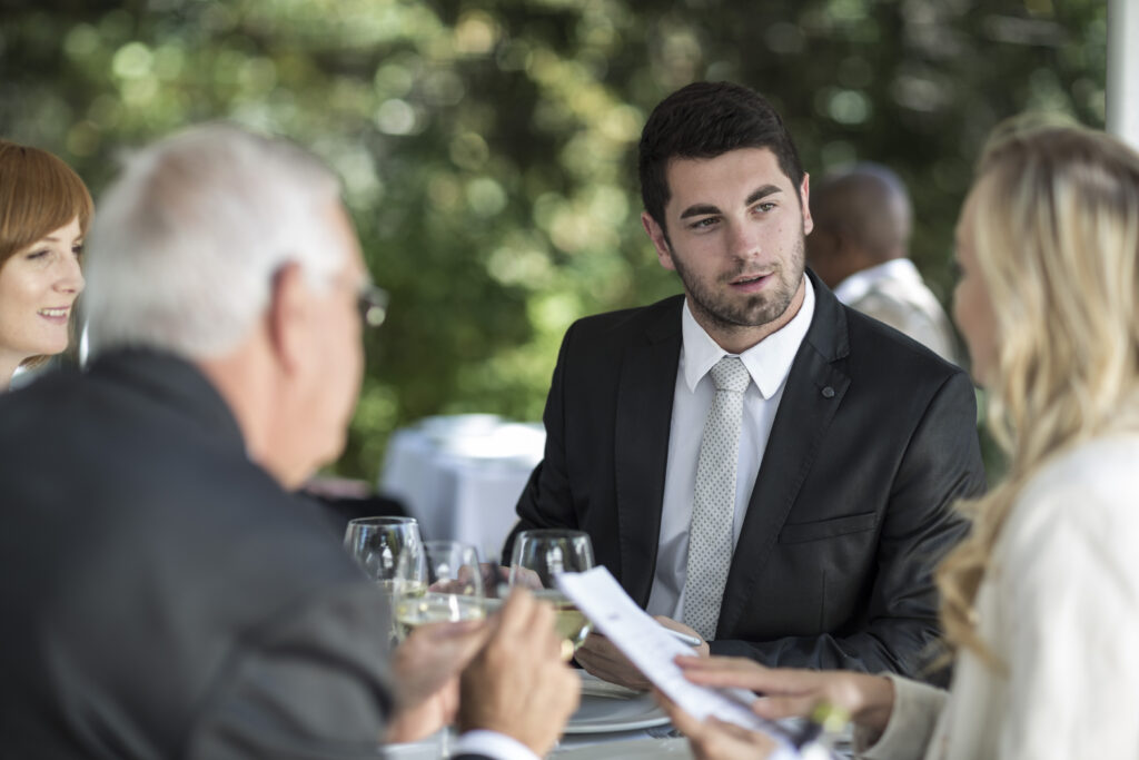 A fundraising representative talking to potential donors in a formal event at an outdoor setting.